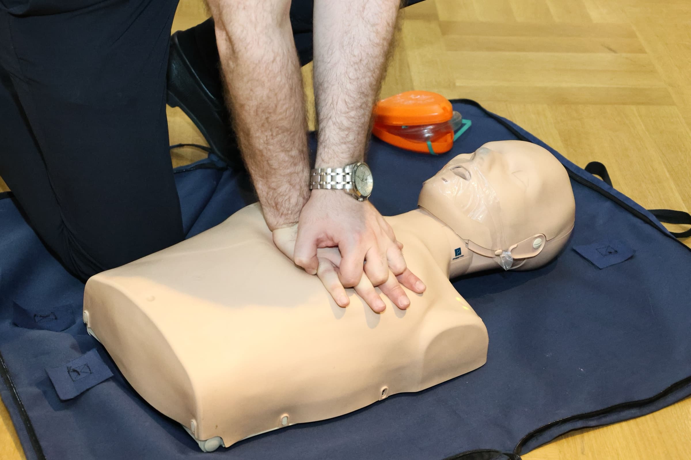 A student performing chest compressions on a CPR manikin beside a pocket mask