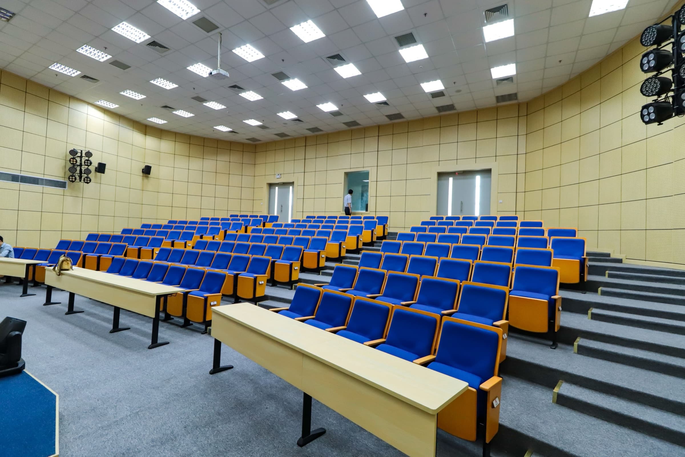 An empty tiered lecture hall with rows of seats and desks
